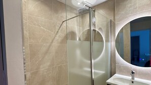 Ein modernes Badezimmer mit Duschkabine aus Glas, einem Waschbecken mit Spiegel und beige gefliesten Wänden.