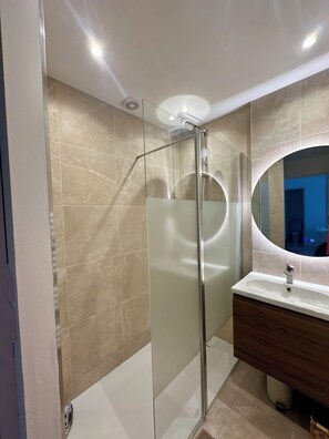 Ein modernes Badezimmer mit Duschkabine aus Glas, einem Waschbecken mit Spiegel und beige gefliesten Wänden.