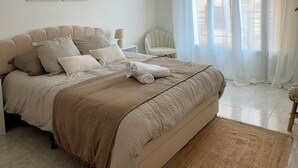 Ein Schlafzimmer mit einem Bett, einem Nachttisch, einem Sessel und einem Fenster mit Vorhängen.