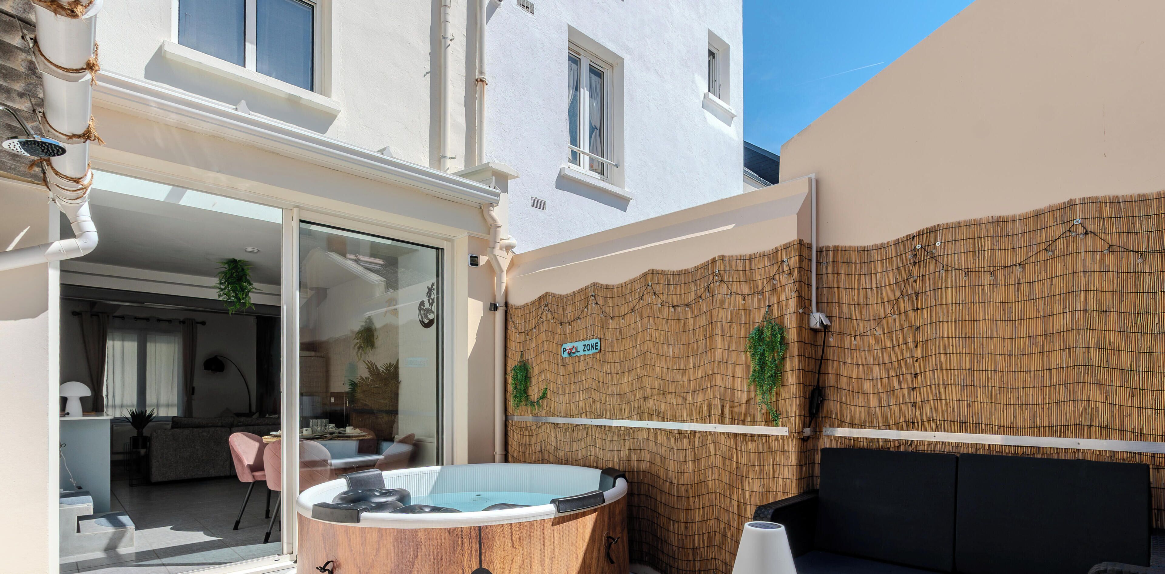 A modern outdoor area with a hot tub, a glass door entrance, and a bamboo wall with a 'POOL ZONE' sign.