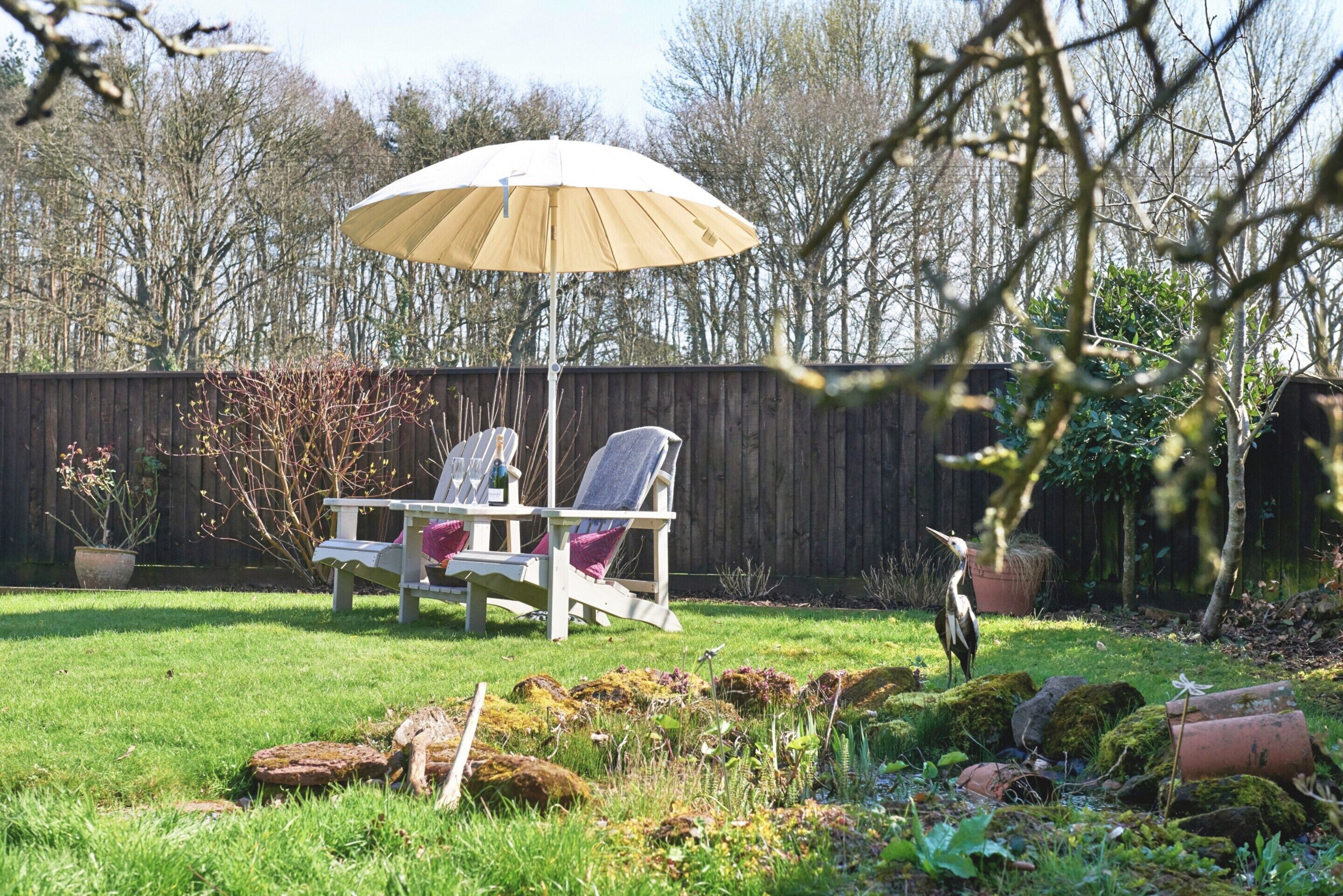 A backyard with two lawn chairs under a large umbrella, a wooden fence, and a bird.