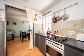 Cozinha com fogão, forno e panelas penduradas. Há uma área de jantar com mesa e cadeiras.