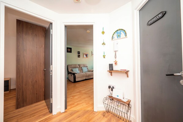 Um corredor com uma porta de madeira, uma porta cinza identificada com 'WASHROOM' e um sofá ao fundo.