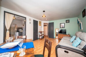 A living room with a sofa, a dining table with chairs, a kitchen area, and a television. - Comfortable Stay in the Heart of Vibrant Deptford - Pass the Keys (London)