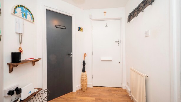 A hallway with a black door labeled 'WASHROOM,' a white door, a radiator, a wicker umbrella, a shelf with a speaker, and a wall-mounted light fixture. - Comfortable Stay in the Heart of Vibrant Deptford - Pass the Keys (London)