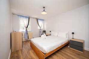 A bedroom with a wooden bed, a nightstand, a dresser, and a window with curtains. - Comfortable Stay in the Heart of Vibrant Deptford - Pass the Keys (London)