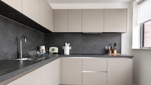 Eine moderne Küche mit dunkler Spritzschutzwand, hellen Schränken, einer Edelstahlspüle und einem Fenster für natürliches Licht.