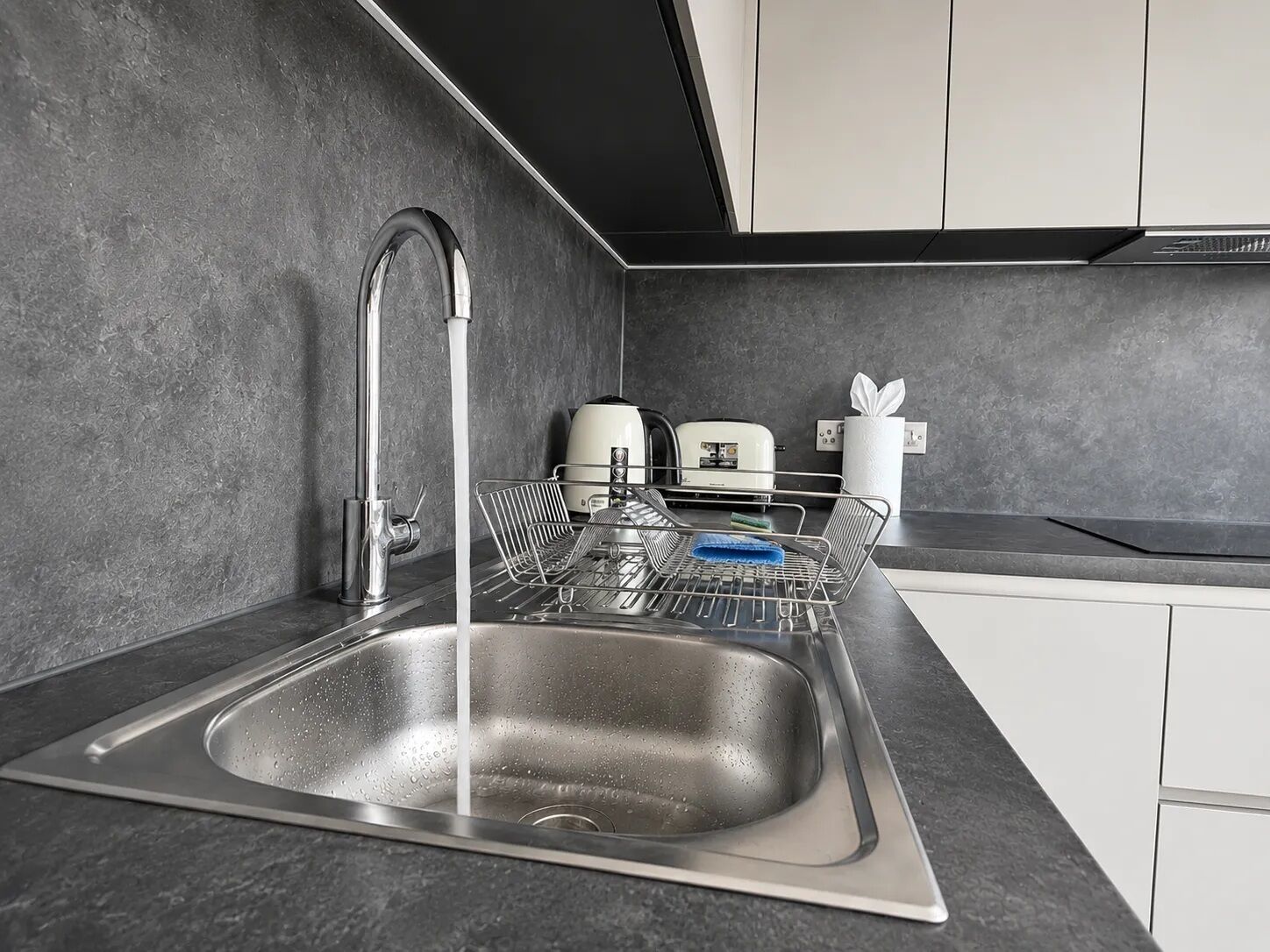 A modern kitchen with a stainless steel sink, a built-in dish rack, a kettle, and a toaster.