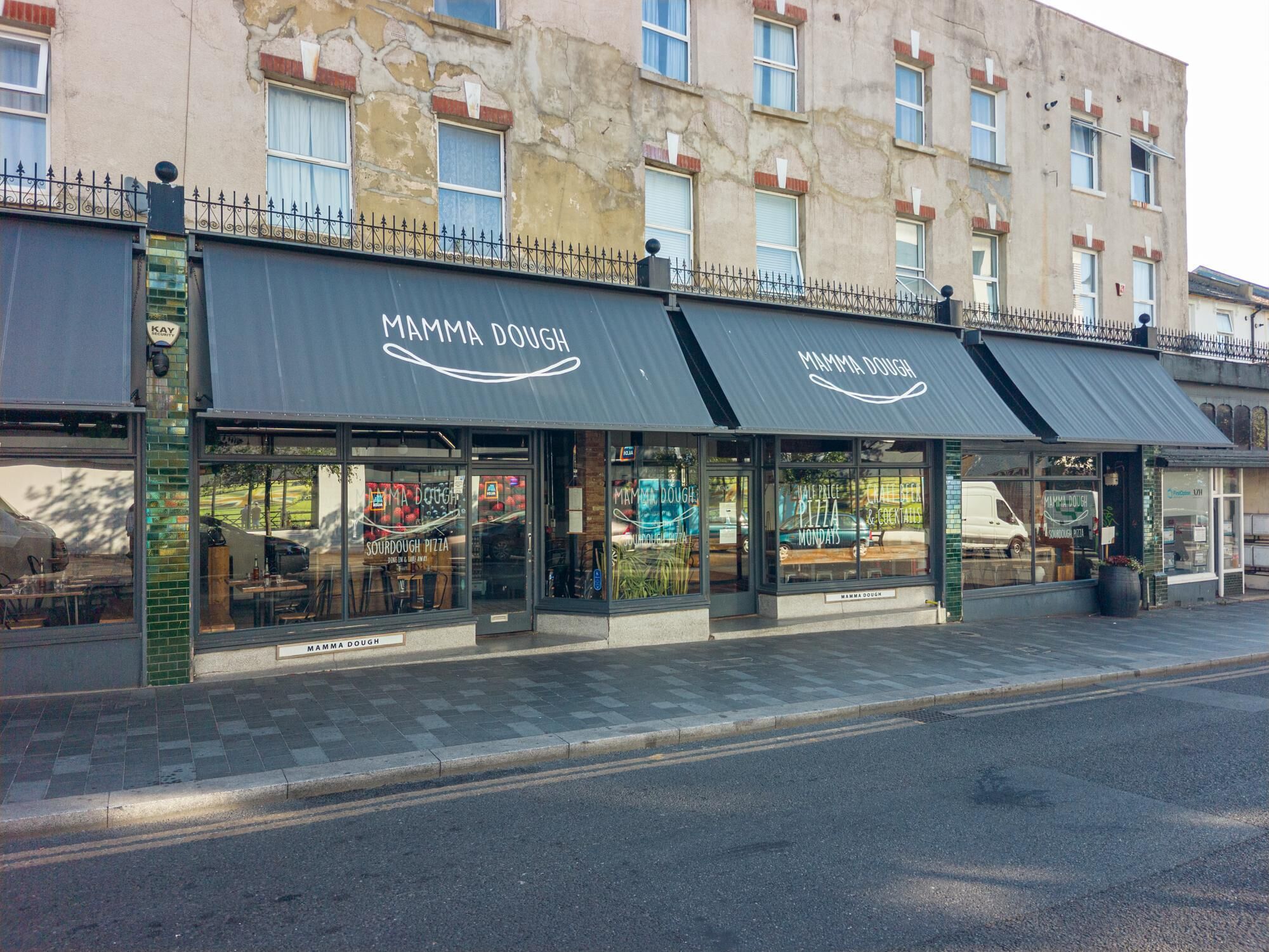 A storefront with a sign reading 'MAMMA DOUGH' and a menu board advertising 'Sourdough Pizza' and 'Cheese & Coctails.'