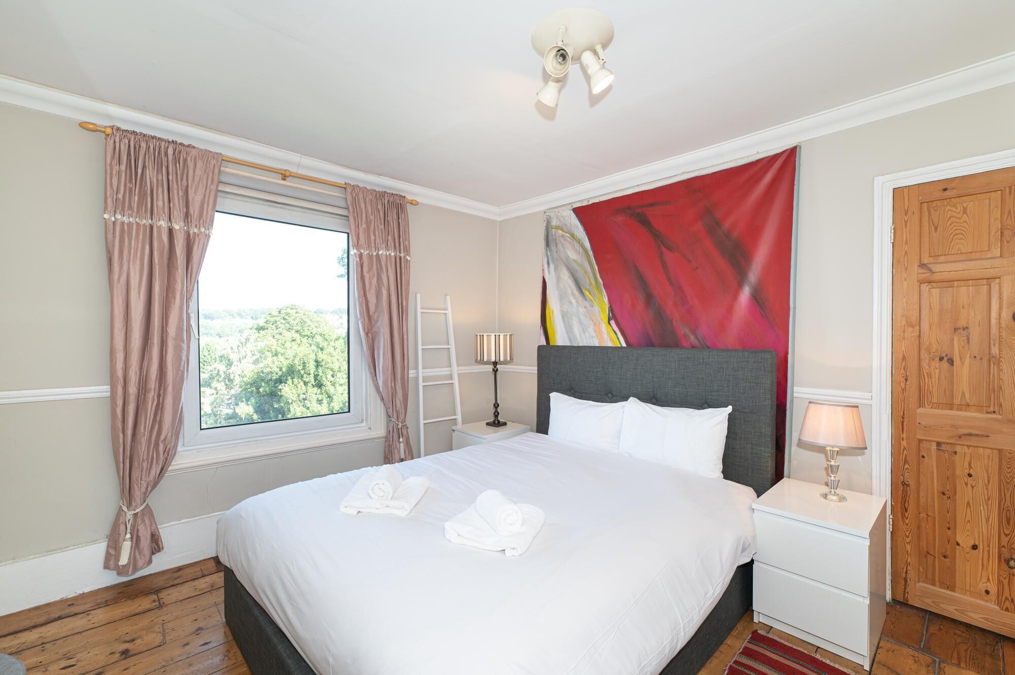 A hotel room with a bed, a window with curtains, a bedside table with a lamp, and a door.
