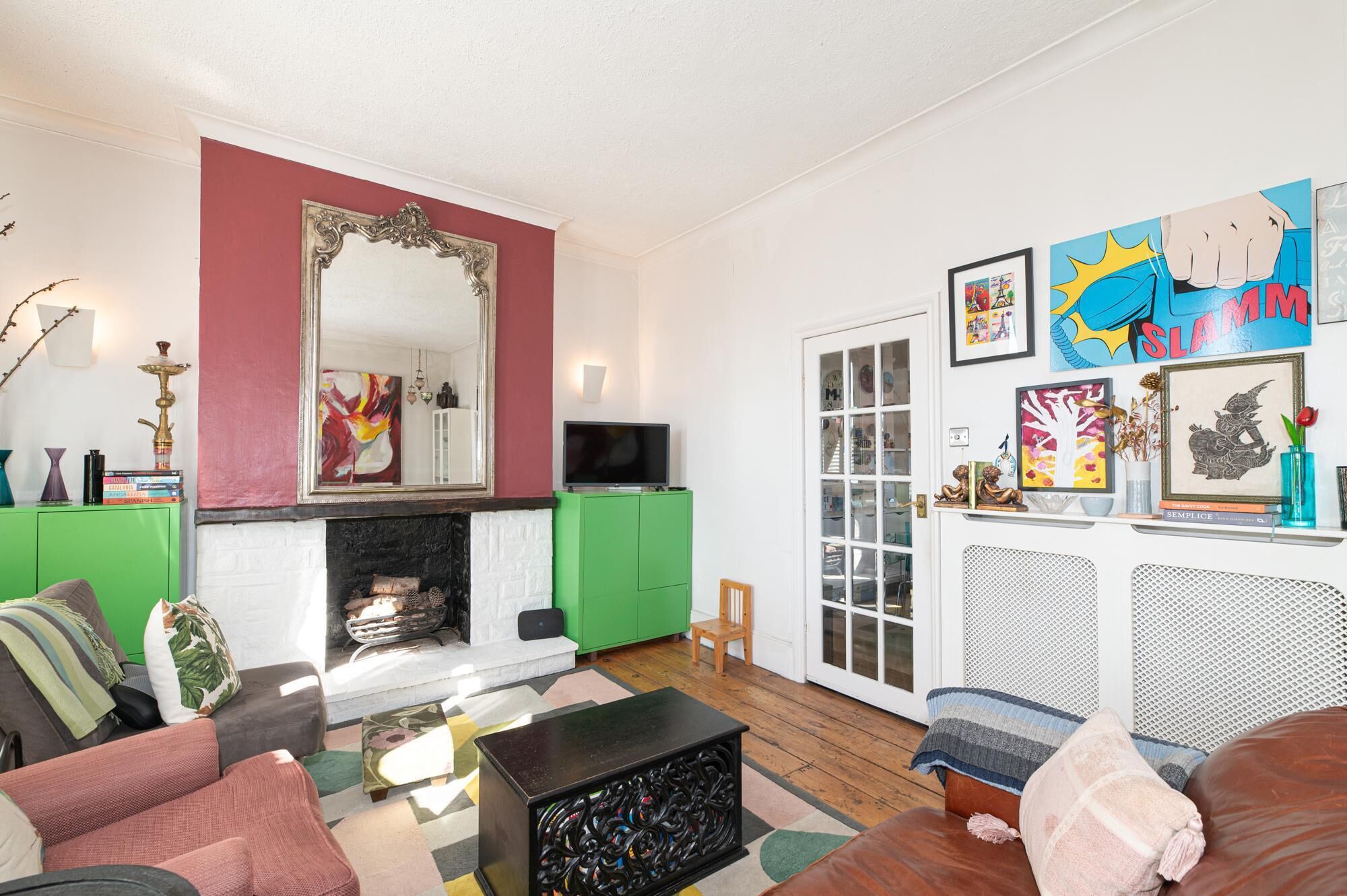 A living room with a fireplace, green cabinets, a television, and various artworks on the walls.