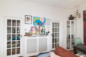 Ein Wohnzimmer mit einem braunen Ledersofa, einer weißen Kommode mit Glastüren und verschiedenen gerahmten Kunstwerken an der Wand.