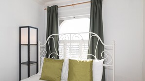 A bed with a metal frame, two pillows, a bedside table, and a window with curtains. - Charming Victorian House, Selhurst Park, London - Pass the Keys (London)