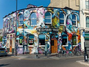 A building with a colorful mural, a sign reading 'The Cherry Tree,' and a storefront with various items on display. - Charming Victorian House, Selhurst Park, London - Pass the Keys (London)