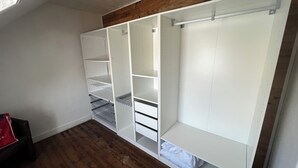 Quarto com teto de madeira, paredes brancas e um armário embutido com várias prateleiras e gavetas.