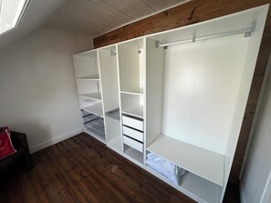 Ein Zimmer mit Holzboden, weißen Wänden und einem Einbauschrank mit mehreren Regalen und Schubladen.