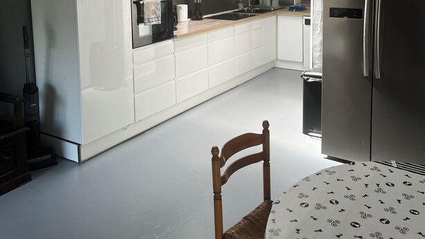 Uma cozinha moderna com armários brancos, uma geladeira de aço inoxidável e uma mesa de jantar com toalha de mesa estampada.