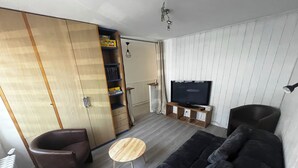 Uma sala de estar com sofá, poltrona, televisão sobre um suporte de madeira e um guarda-roupa com porta deslizante.