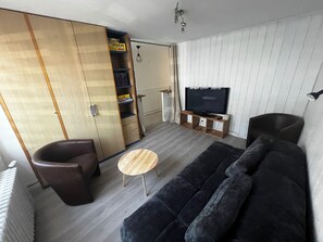 Ein Wohnzimmer mit einer Couch, einem Sessel, einem Fernseher auf einem Holzboden und einem Schrank mit Schiebetür.