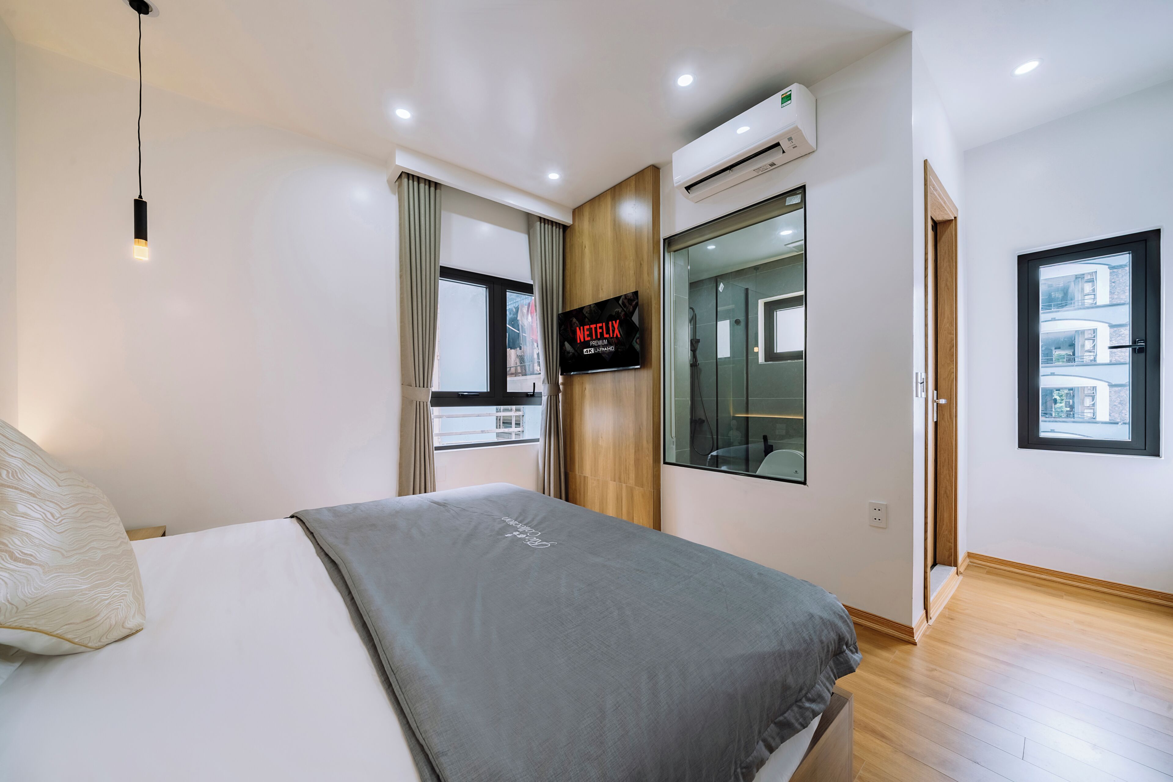 Una habitación de hotel moderna con una cama, un televisor montado en la pared, un equipo de aire acondicionado y una ventana con vistas.