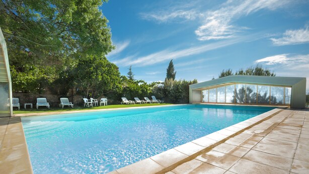 Una piscina amb aigua clara i blava, envoltada per una terrassa de rajola i una zona coberta amb caires.