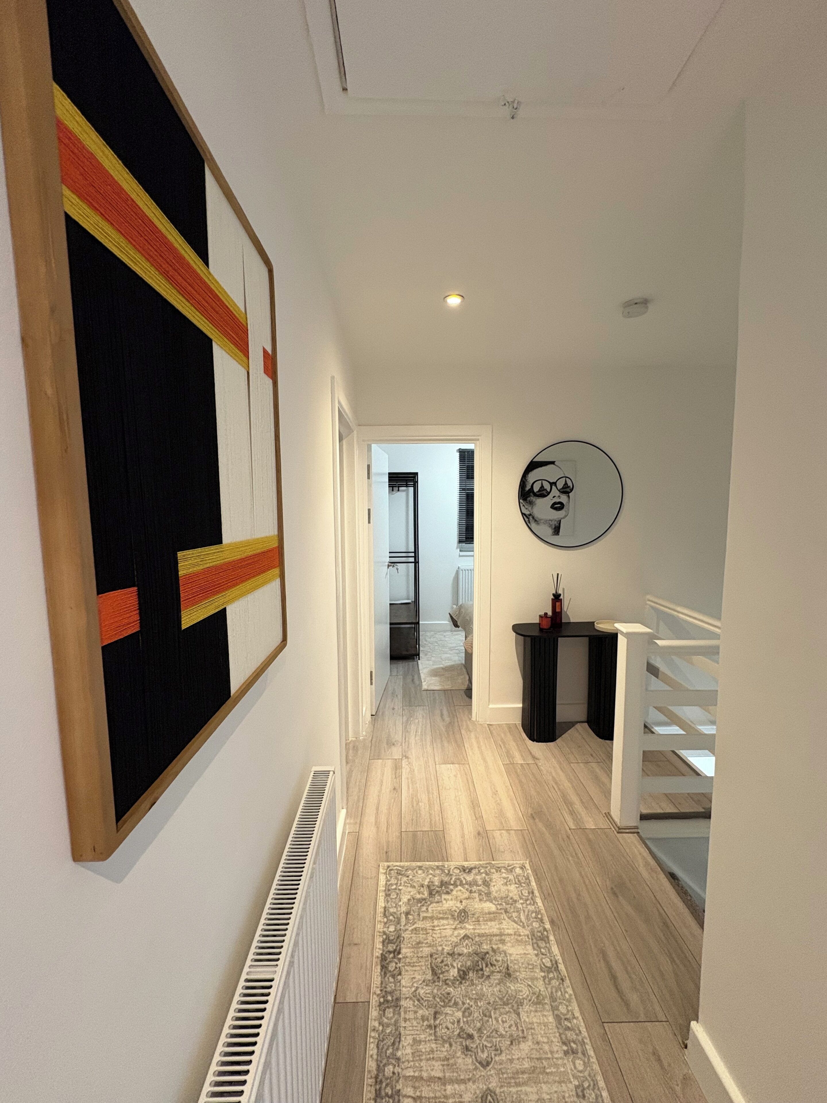 Un pasillo con un radiador, un tapete, una obra de arte enmarcada y una escalera.
