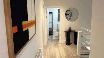 A hallway with a radiator, a rug, a framed artwork, and a staircase.
