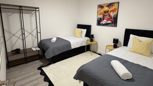 A hotel room with two beds, a wardrobe, a painting, and a ceiling light. - Modern 3 bedroom Apartment, Sleep 5 (Barnet)