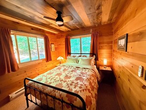 A wooden cabin bedroom with a bed, two bedside lamps, a ceiling fan, and a window with curtains. - Green Wolf Lodge-Peaceful, 3-Bedroom Cabin on Spider Lake Chain near Hayward (Hayward)