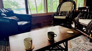 Ein Zimmer mit einem Holztisch, zwei Stühlen und Blick auf Bäume durch große Fenster.