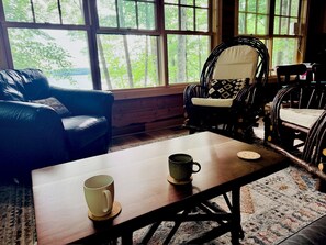 A room with a wooden coffee table, two chairs, and a view of trees through large windows. - Green Wolf Lodge-Peaceful, 3-Bedroom Cabin on Spider Lake Chain near Hayward (Hayward)