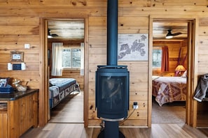 Eine Holzhütte mit einem zentralen Kaminofen, zwei Betten mit gemusterten Bettbezügen und einer Karte an der Wand.