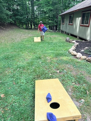 A yard with a wooden structure, a house, and a person carrying a blue object. - Green Wolf Lodge-Peaceful, 3-Bedroom Cabin on Spider Lake Chain near Hayward (Hayward)