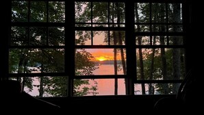 Ein Fenster mit Blick auf einen Sonnenuntergang über einem Gewässer, umrahmt von Bäumen.