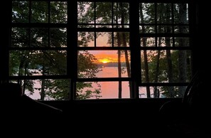 Ein Fenster mit Blick auf einen Sonnenuntergang über einem Gewässer, umrahmt von Bäumen.