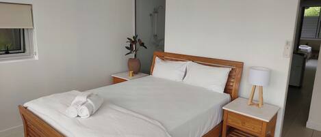 Un lit bien fait, avec du linge de lit blanc, une tête de lit en bois et une table de chevet sur laquelle se trouve une lampe.