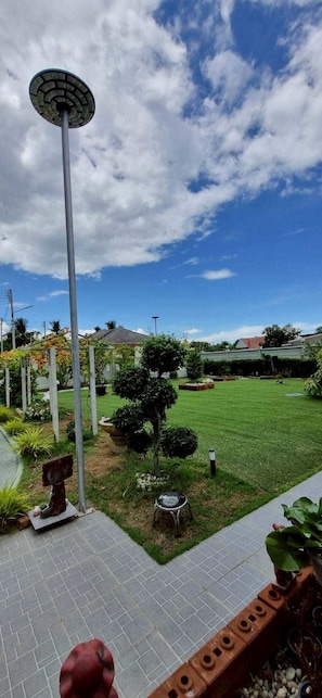 Um jardim ajardinado com um caminho pavimentado, um poste de luz e diversas plantas e arbustos.