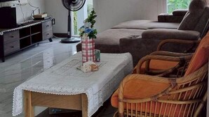 Una sala de estar con televisión de pantalla plana, un reloj de pared grande, un ventilador y un sofá.
