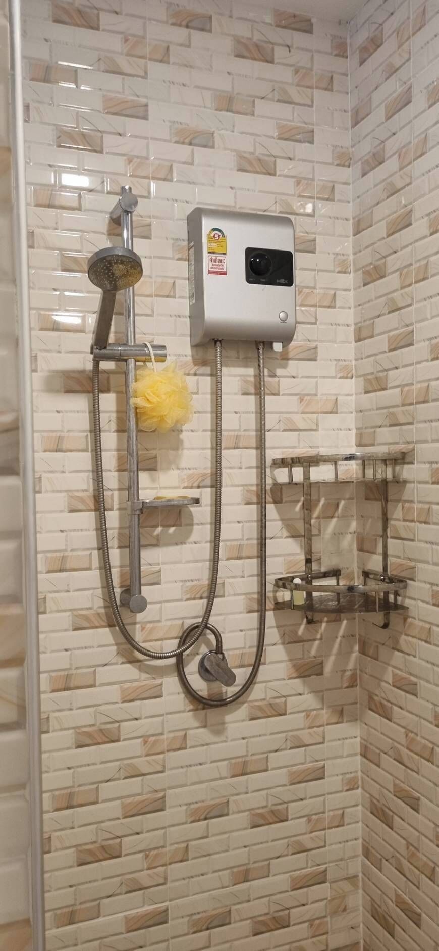 A shower with a handheld showerhead, a wall-mounted control panel, and a yellow sponge.
