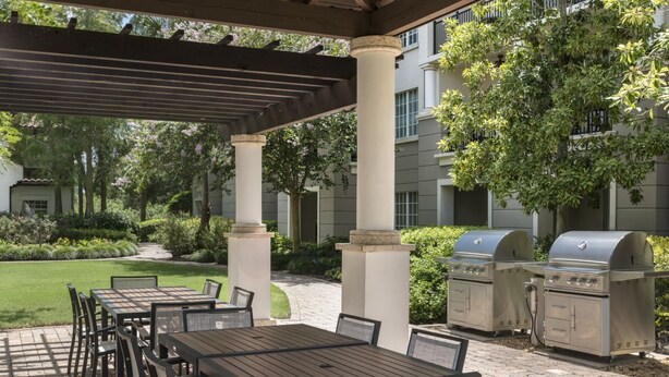 An outdoor patio with tables and chairs, a pergola, and barbecue grills. - 1 Bedroom Villa at Lakeshore Reserve w/ Amenities (Orlando)