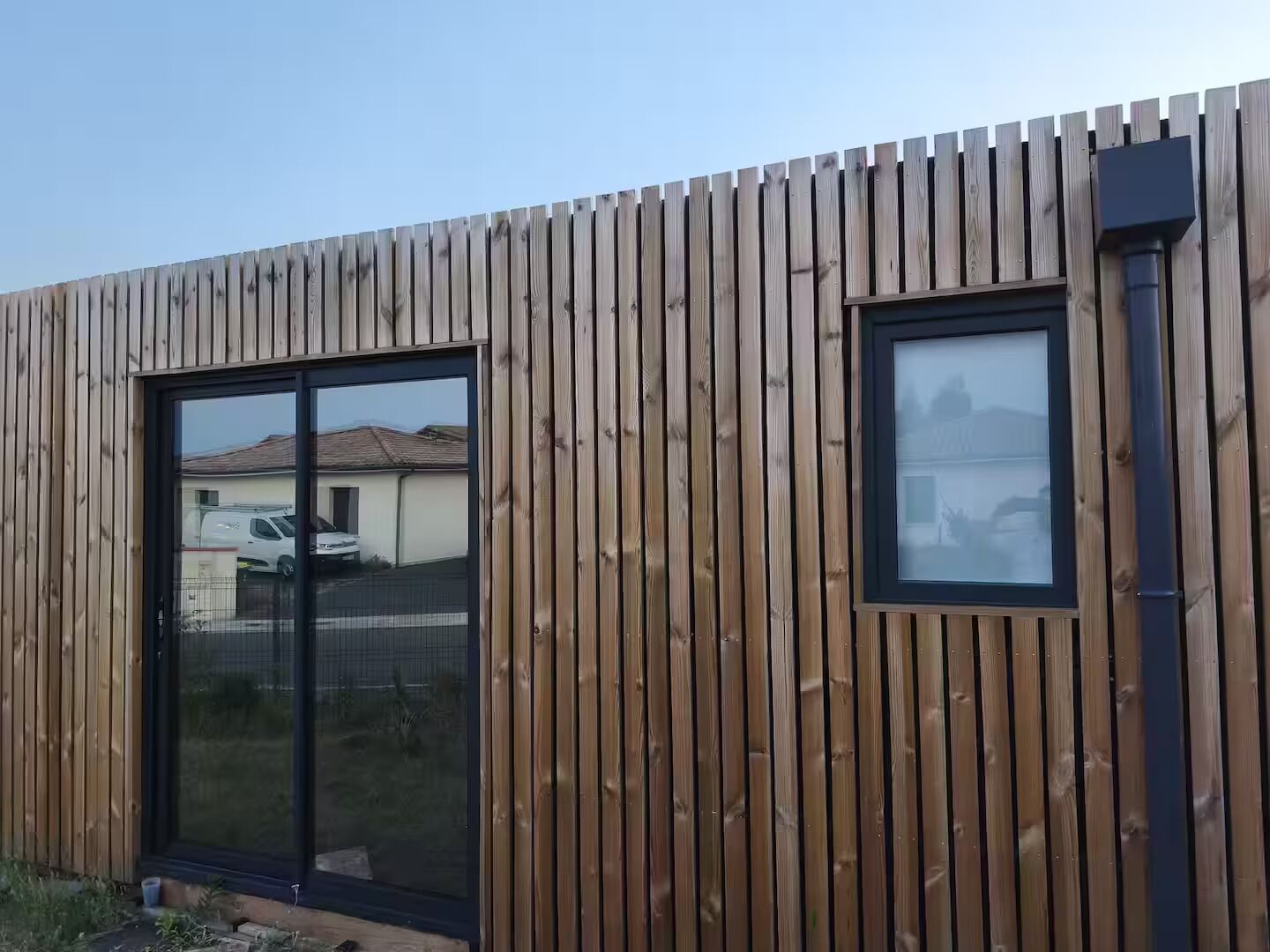 Un edificio moderno con fachada de madera, un amplio cerramiento de vidrio corredero y una ventana pequeña.