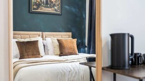 Ein Hotelzimmer mit Bett, Kissen, Nachttisch mit Kaffeemaschine und einem gerahmten Bild an der Wand.