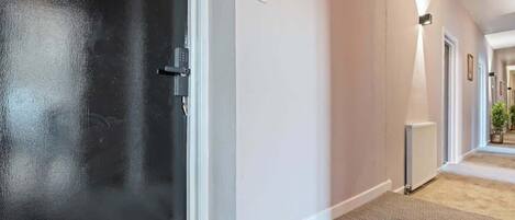 A hallway with a black door, a white wall with a blue sign, and a radiator.