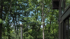 An outdoor seating area with two chairs and a table, surrounded by a wooden structure, with trees in the background.