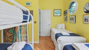 Une chambre avec un lit superposé, deux lits simples, une porte et divers tableaux encadrés accrochés aux murs.