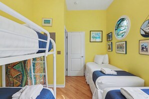 A room with a bunk bed, two single beds, a door, and various framed pictures on the walls. - Sleepy Hollow Beach Resort, Villa E – Family Fun on Lake Michigan! (South Haven)