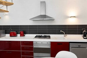 Una cucina moderna con piano cottura a gas, forno integrato, lavastoviglie e una combinazione di colori rosso e bianco.