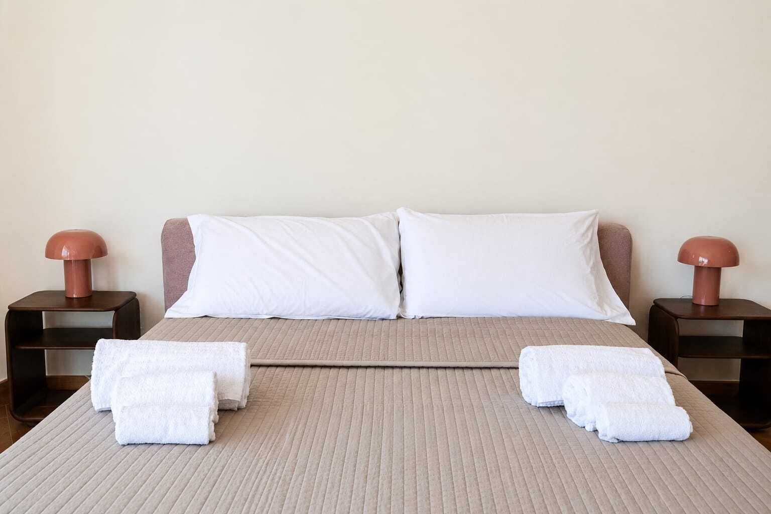 Un letto ben rifatto con due cuscini, un asciugamano piegato e due comodini con lampade.