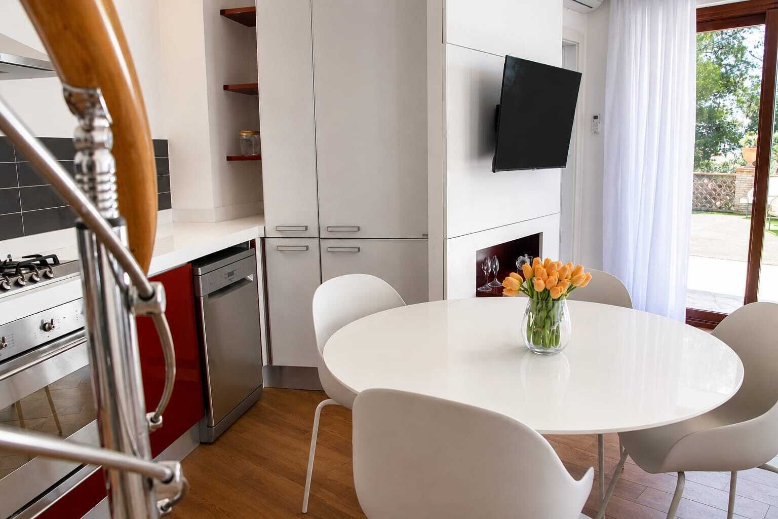 A modern kitchen with white cabinets, a built-in oven, and a dining area with a white table and chairs.
