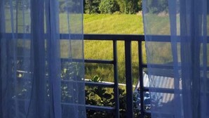 A room with a large window, curtains, and a view of a green field.